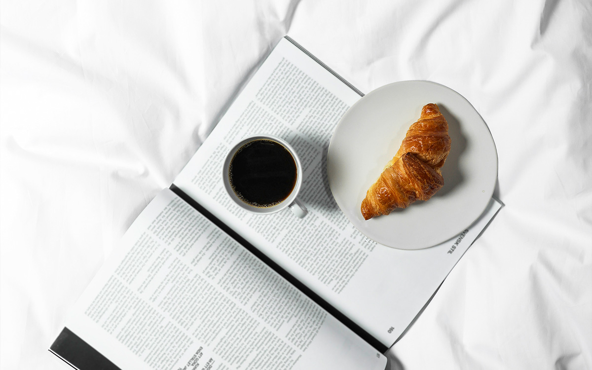 Säng med bok, kaffe och fika